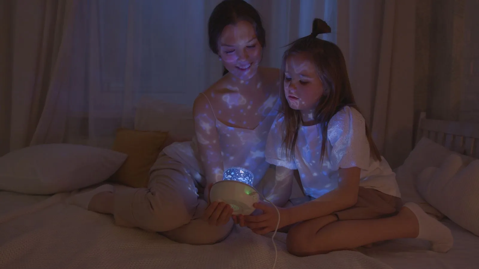 Mãe e filha no quarto escuro olhando uma luminária de estrelas
